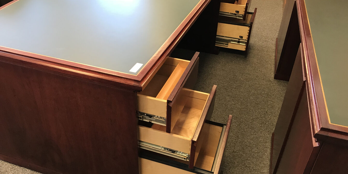 A large wooden desk with drawers and a green top.